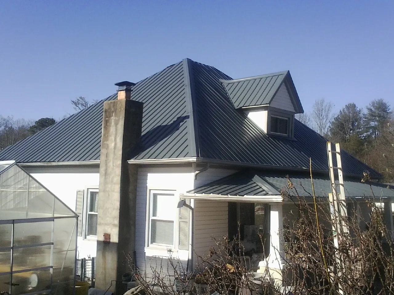 Dark blue standing seam metal roof on a white farmhouse with dormer — Slate & Tile Roof Repair by Roofing Brothers in Pinellas Park