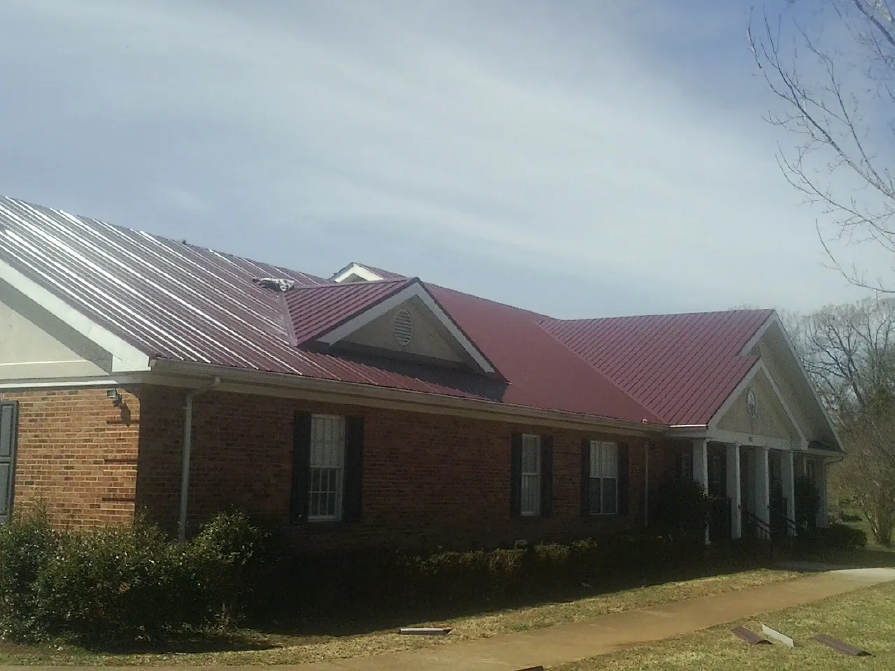 Red metal roof with gabled entries on a long brick building, from a Hail Damage Roof Repair job in Pinellas Park