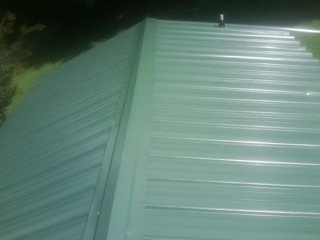 New green metal panels meeting at the ridge of a roof — Flat Roof Repair work by our crew in Pinellas Park