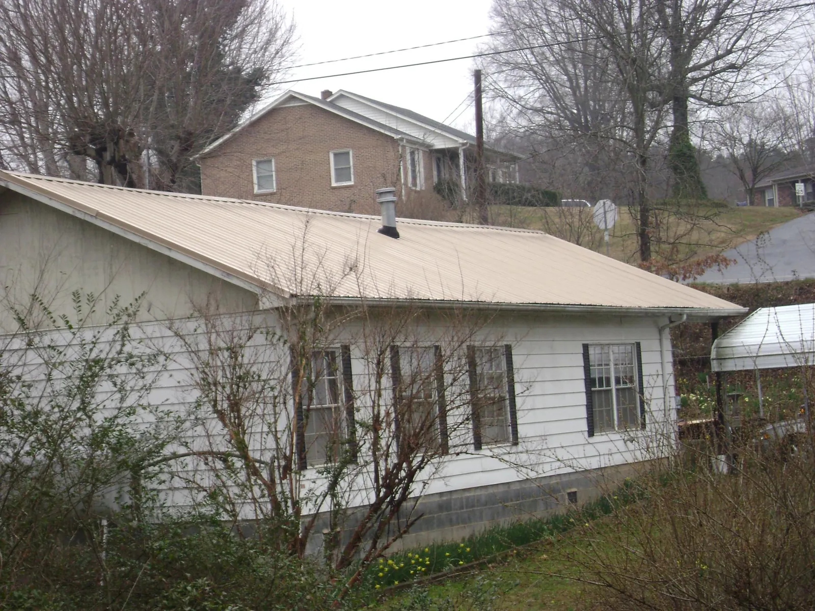 Tan metal roof on a white sided house set into a hillside — Commercial Roofing by Roofing Brothers in Pinellas Park